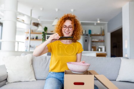 Photo for Young satisfied happy woman shopaholic customer sit on sofa unpack parcel delivery box, online shopping shipment concept. taking photos of product to post on social media - Royalty Free Image