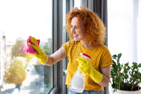 Téléchargez les photos : Housework and housekeeping concept - happy woman in gloves cleaning window with rag and cleanser spray at home - en image libre de droit