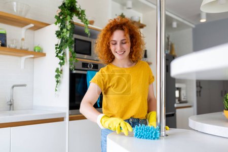 Porträt einer schönen Hausfrau, die mit schützenden gelben Handschuhen Staub reinigt. Frau freut sich über Putzkonzept