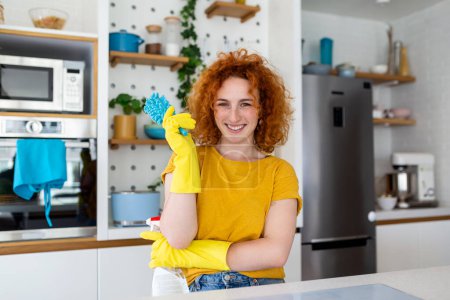 Foto de Young woman doing house chores holding cleaning tools. Woman wearing rubber protective yellow gloves, holding rag and spray bottle detergent. It's never too late to clean - Imagen libre de derechos