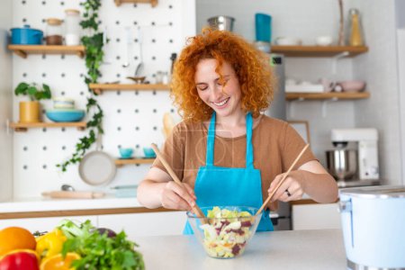 Téléchargez les photos : Belle jolie jeune femme souriante sur la cuisine prépare une salade végétalienne en vêtements décontractés
. - en image libre de droit