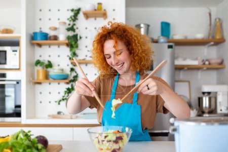 Foto de Hermosa linda joven sonriente mujer en la cocina está preparando una ensalada vegana en ropa casual
. - Imagen libre de derechos