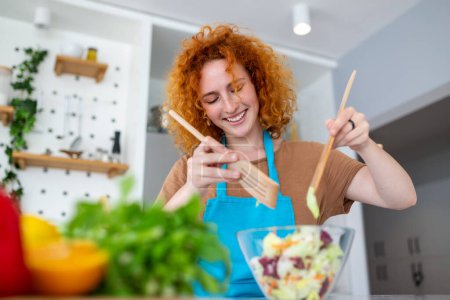 Téléchargez les photos : Belle jolie jeune femme souriante sur la cuisine prépare une salade végétalienne en vêtements décontractés
. - en image libre de droit