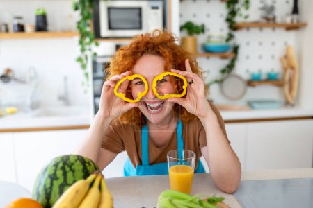 Foto de Foto de mujer joven sonriendo mientras cocina ensalada con verduras frescas en el interior de la cocina en casa - Imagen libre de derechos