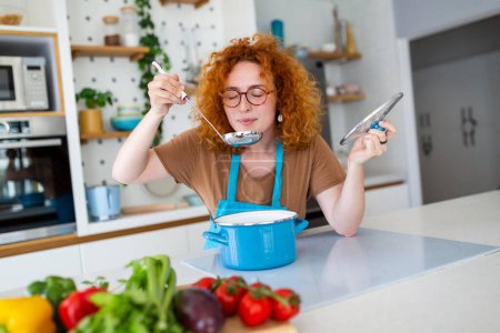 Young smiling woman enjoying in taste and smell while cooking lunch in the kitchen.