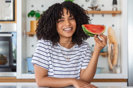 Photo for Image of cheerful young woman eating watermelon in the kitchen at home - Royalty Free Image