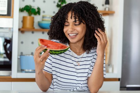 Photo for Beautiful African Mother eating Watermelon at Home Kitchen - Royalty Free Image