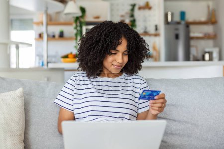 Foto de Young woman holding credit card and using laptop computer. Online shopping concept. Happy woman doing online shopping at home - Imagen libre de derechos