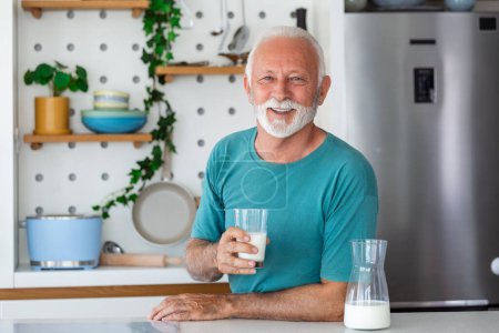 Photo for Senior man drinking a glass of milk with a happy face standing and smiling. Handsome senior man drinking a glass of fresh milk in the kitchen - Royalty Free Image