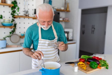 Téléchargez les photos : Heureux homme âgé qui s'amuse à cuisiner à la maison - Personne âgée qui prépare un déjeuner santé dans une cuisine moderne - Temps de vie à la retraite et concept de nutrition alimentaire - en image libre de droit