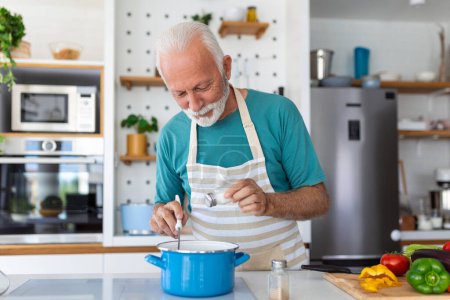 Photo for Happy senior man having fun cooking at home - Elderly person preparing health lunch in modern kitchen - Retired lifestyle time and food nutrition concept - Royalty Free Image