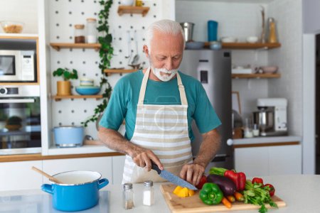Glücklicher Rentner kocht in der Küche. Ruhestand, Hobbymenschen-Konzept. Porträt eines lächelnden Seniors beim Gemüseschneiden