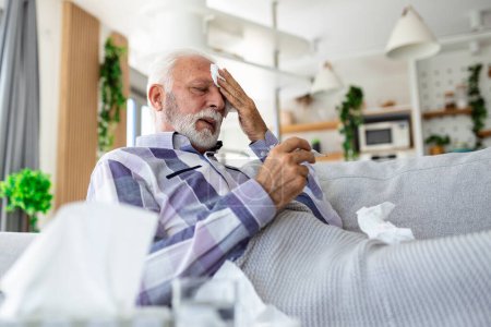 Photo for Sick elderly man checking his temperature suffering from seasonal flu or cold lying on sofa caughing suffering from seasonal flu or cold. . Ill senior feel unhealthy with influenza at home - Royalty Free Image