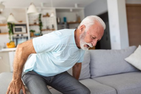 Foto de Anciano mayor tocándose la espalda, sufriendo de dolor de espalda, ciática, sedentarismo. Problemas de salud de la columna. Asistencia sanitaria, seguros - Imagen libre de derechos