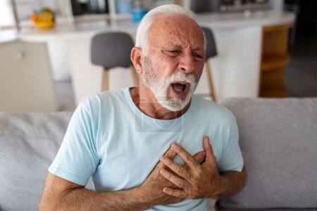 Photo for Senior man presses hand to chest has heart attack suffers from unbearable pain, Mature man with pain on heart in living room. Senior man suffering from bad pain in his chest heart attack at home - Royalty Free Image