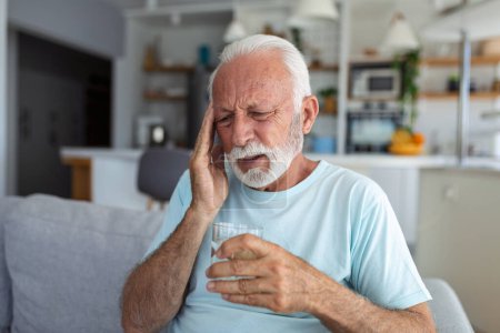 Photo for Senior man suffering from a headache at home. Worried senior man sitting alone in his home. This headache really hurts. My head is killing me - Royalty Free Image
