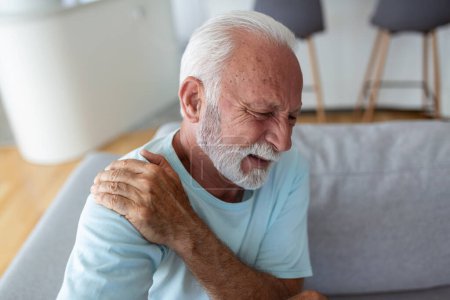 Foto de Anciano mayor tocándose el hombro, sufriendo de dolor en el hombro, ciática, sedentarismo. problemas de salud del hombro. Asistencia sanitaria, seguros - Imagen libre de derechos