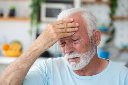 Photo for Tired, depressed senior man sitting on couch in living room feeling hurt and lonely. Aged, white-haired man touching forehead suffering from severe headache or recalling bad memories - Royalty Free Image