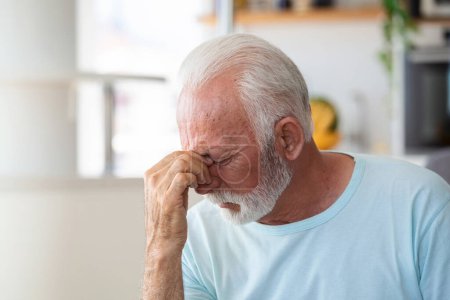 Photo for Tired, depressed senior man sitting on couch in living room feeling hurt and lonely. Aged, white-haired man touching forehead suffering from severe headache or recalling bad memories - Royalty Free Image