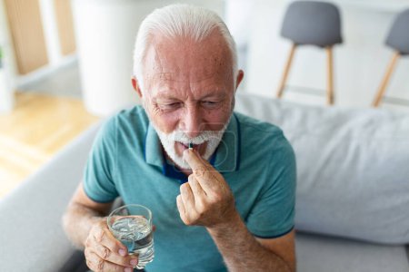 Téléchargez les photos : Homme âgé prend la pilule avec un verre d'eau à la main. Homme mature stressé buvant des médicaments antidépresseurs sédatés. L'homme se sent déprimé, il se drogue. Médicaments au travail - en image libre de droit