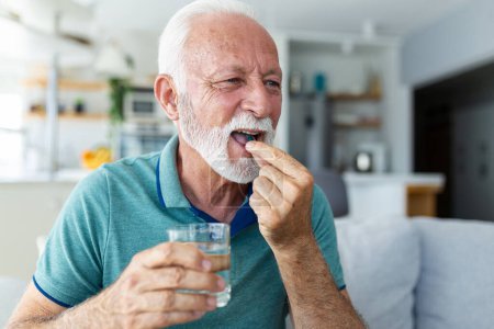 Téléchargez les photos : Homme âgé prend la pilule avec un verre d'eau à la main. Homme mature stressé buvant des médicaments antidépresseurs sédatés. L'homme se sent déprimé, il se drogue. Médicaments au travail - en image libre de droit