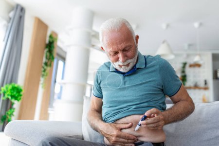Téléchargez les photos : Homme âgé assis sur le canapé et s'injectant de l'insuline pour son diabète - en image libre de droit