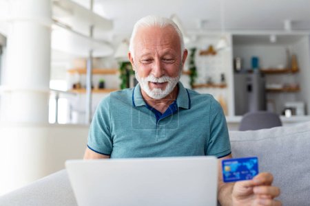 Photo for Mature man using laptop, holding plastic credit or debit card, senior grey haired customer making secure internet payment, shopping or browsing online banking service, entering information - Royalty Free Image