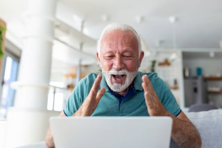 Photo for Elderly man seated on couch looking at laptop screen scream with joy feels excited happy celebrating lottery victory, lucky moment, got online opportunity, sales and discounts e-commerce concept - Royalty Free Image