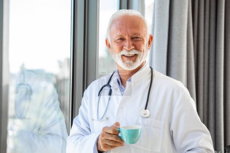 Téléchargez les photos : Portrait de professionnel de la santé mature senior, médecin, avec stéthoscope tenant tasse bleue de café, - en image libre de droit