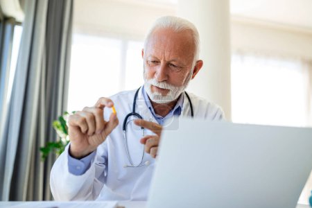 Photo for Doctor online. Senior medic talking to client on laptop computer from his office. Mature male therapist explaining medical treatment to patient through a video call with laptop in the consultation. - Royalty Free Image