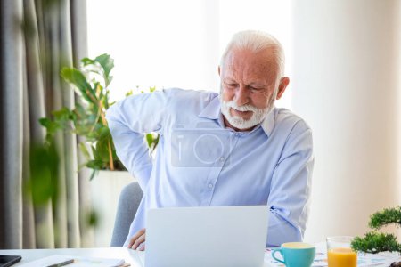 Photo for Senior businessman working sitting at desk suffers from lower back pain. Damage of intervertebral discs, spinal joints, compression of nerve roots caused by wrong posture and sedentary work - Royalty Free Image