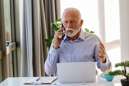 Photo for Mature businessman working on laptop and talking on cellphone. Handsome mature business leader sitting in a modern office - Royalty Free Image