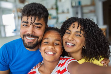 Téléchargez les photos : Famille africaine heureuse avec fille s'amuser avec gadget sur le canapé en utilisant un smartphone à la maison, les parents et les enfants font selfie appel vidéo sur l'application en ligne téléphone - en image libre de droit