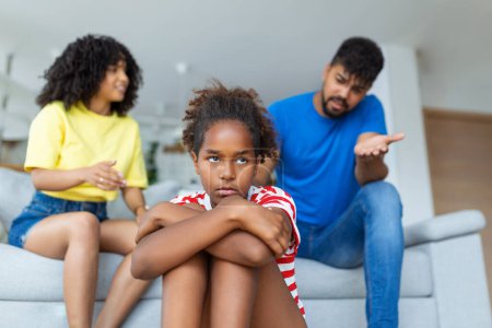 Photo for Family Misunderstanding, Childhood Problems. Sad offended black daughter sitting on the floor, turning back to parents after quarrel at home, upset mom and dad asking resentful girl what's wrong - Royalty Free Image