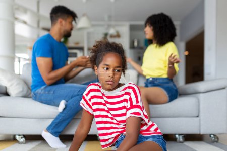 Photo for Divorce And Domestic Violence. Portrait of upset African American daughter looking through the window while her angry parents fighting in the background, depressed child feeling lonely - Royalty Free Image