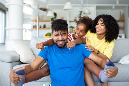 Photo for Happy African American dad and mom with excited proud daughter kid, playing flying superhero, reaching arm forward. Cheerful girl playing active game with family at home - Royalty Free Image