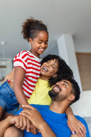 Photo for Happy dad and mom with their cute daughter hug and have fun sitting on the sofa in the living room at home. - Royalty Free Image