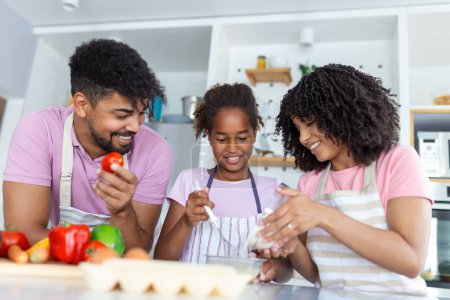 Photo for Shot of beautiful cute family having fun while cooking together in the kitchen at home. Cute little girl and her beautiful parents are smiling while cooking in kitchen at home - Royalty Free Image