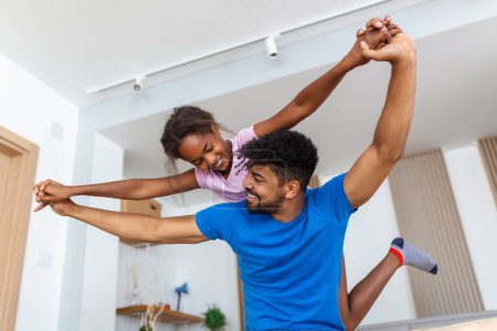Foto de Familia feliz divirtiéndose en casa, jóvenes padres afroamericanos jugando con su pequeña hija en la sala de estar, mamá, papá e hijo sonriendo y riendo - Imagen libre de derechos