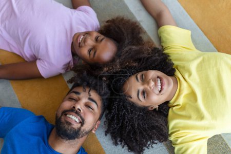 Téléchargez les photos : Affectueux afro-américains parents et fille mignonne riant couché sur le sol ensemble, heureux mixte famille avec des liens pour enfants avoir du plaisir profiter de moments drôles dans la chambre, vue du dessus - en image libre de droit