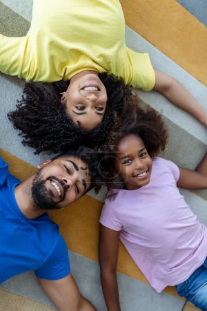 Photo for Family weekend. Smiling black mother, father and daughter lying on bed together, relaxing at home. - Royalty Free Image