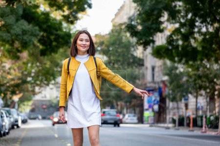 Photo for Young woman hailing a taxi ride. Beautiful charming woman hailing a taxi cab in the street. Businesswoman trying to hail a cab in the city. Tourist woman hailing a taxi - Royalty Free Image