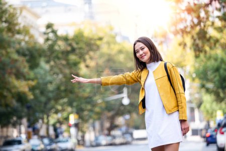 Photo for Young Asian woman hailing a taxi ride. Beautiful charming woman hailing a taxi cab in the street. Businesswoman trying to hail a cab in the city. Tourist woman hailing a taxi - Royalty Free Image