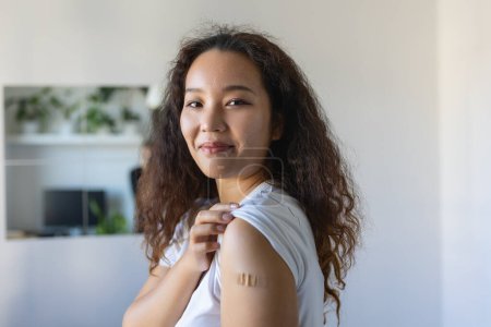 Photo for Young Asian woman with adhesive bandage on her arm after Corona virus vaccine. First aid. Medical, pharmacy and healthcare concept. - Royalty Free Image