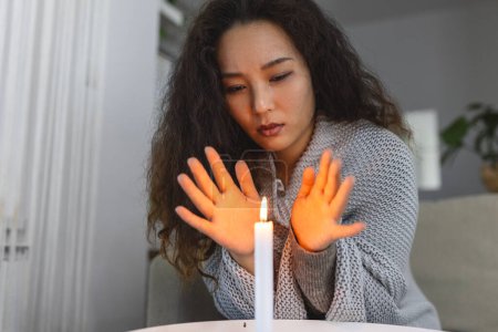 Téléchargez les photos : Burning candle, women trying to heat her hands in dark home. Shutdown of heating and electricity, power outage, blackout, load shedding or energy crisis - en image libre de droit