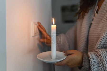 Foto de Energy crisis. Hand in complete darkness holding a candle trying to turn on light during a power outage. Blackout concept. - Imagen libre de derechos