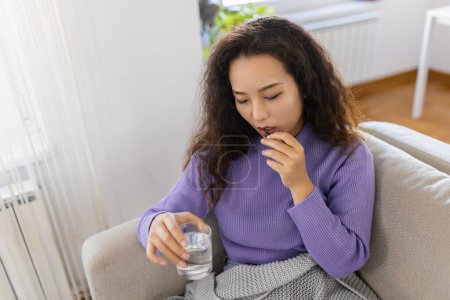 Photo for Asian ill sick woman taking painkiller medicine to relieve stomachache pain sit on bed in the morning. Sick woman lying in bed with high fever. Cold flu and migraine. - Royalty Free Image