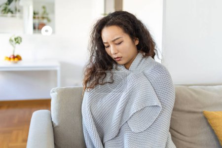 Téléchargez les photos : Sick young Asian woman feeling cold covered with blanket sit on bed, ill black girl shivering freezing warming at home wrapped with plaid, no central heating problem, fever temperature flu concept - en image libre de droit