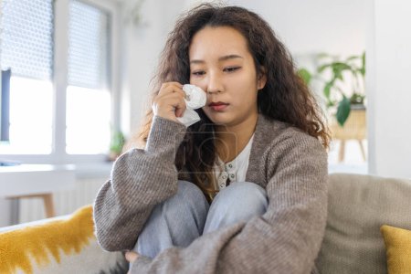 Photo for Unhappy young Asian woman crying alone close up, depressed girl sitting on couch at home, health problem or thinking about bad relationships, break up with boyfriend, divorce - Royalty Free Image