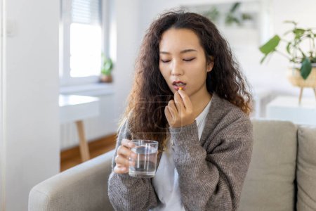 Foto de Asian woman takes medicines with glass of water. Daily norm of vitamins, effective drugs, modern pharmacy for body and mental health concept - Imagen libre de derechos